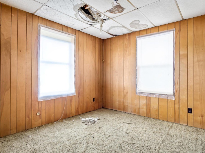 Carpeted empty room with a drop ceiling and wooden walls