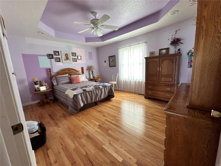 Bedroom featuring a ceiling fan, a raised ceiling, a textured ceiling, baseboards, and hardwood floors