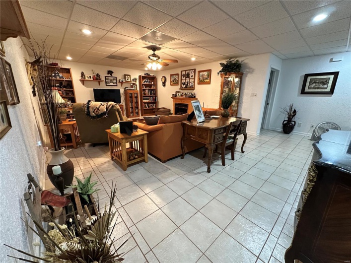 Living room featuring a drop ceiling, a ceiling fan, light tile  floors, and baseboards