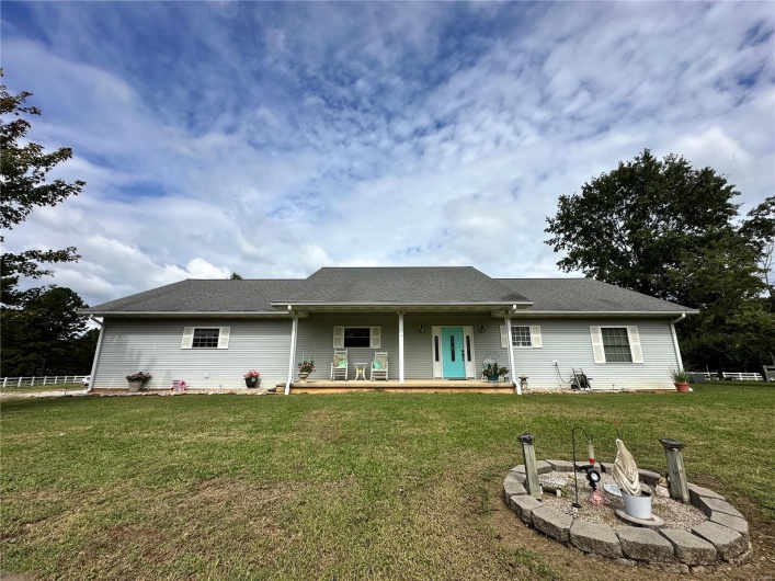 Back of property with a porch, a fire pit, roof with shingles, and a lawn