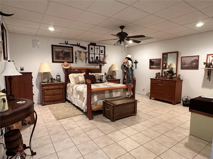 Bedroom featuring a drop ceiling, light tile patterned floors, baseboards, and a ceiling fan