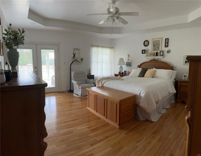 Bedroom with access to outside, a ceiling fan, a raised ceiling, hardwood floors, and french doors