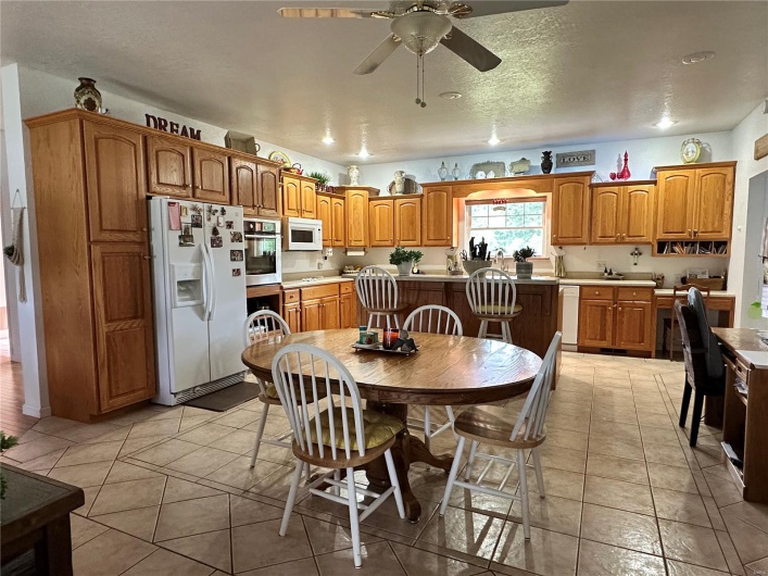 Kitchen with light countertops, a ceiling fan, brown cabinetry, and white appliances