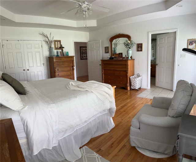 Bedroom with a tray ceiling, a closet, light hardwood floors, ceiling fan, and a textured wall