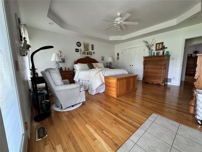 Bedroom with a tray ceiling, hardwood flooring, ceiling fan, visible vents, and a closet