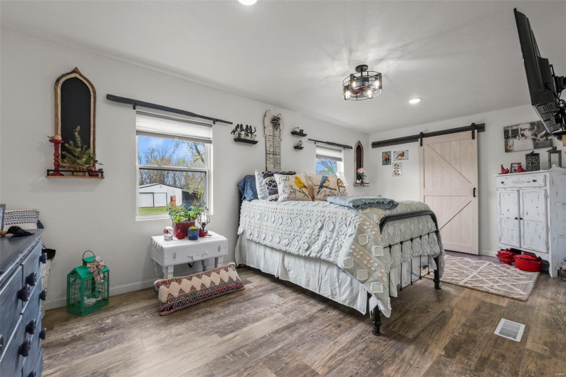 Bedroom with a barn door, wood finished floors, baseboards, visible vents, and recessed lighting