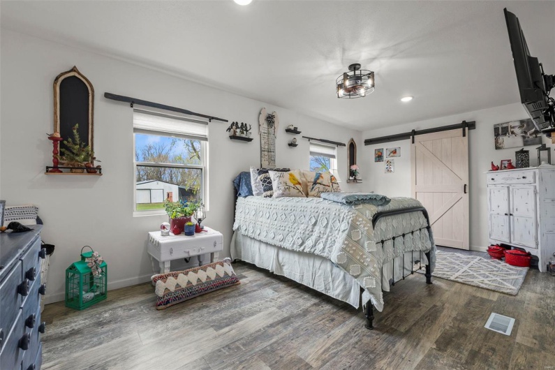 Bedroom featuring visible vents, baseboards, wood finished floors, recessed lighting, and a barn door