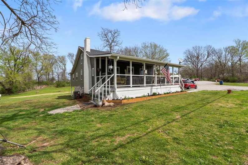 View of front of property with gravel driveway, a front lawn, covered porch, central AC, and a chimney