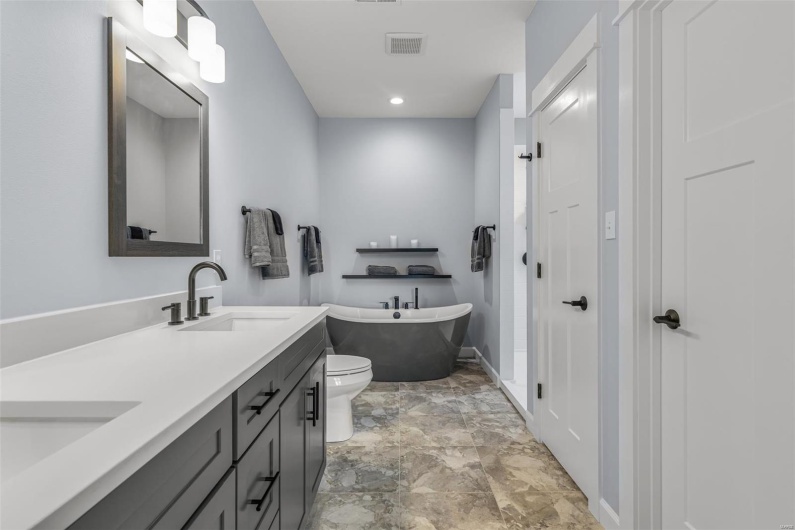 Bathroom with toilet, a sink, visible vents, a freestanding bath, and double vanity