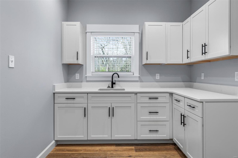 Kitchen featuring light countertops, baseboards, a sink, white cabinets, and wood finished floors