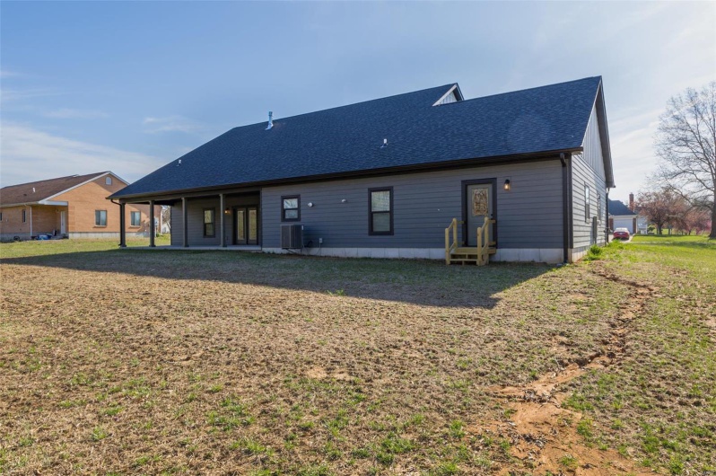 Rear view of house featuring entry steps, a shingled roof, central AC, and a yard