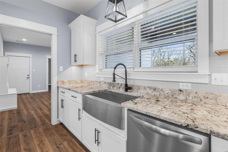 Kitchen with tasteful backsplash, dark wood-type flooring, stainless steel dishwasher, a sink, and light stone countertops