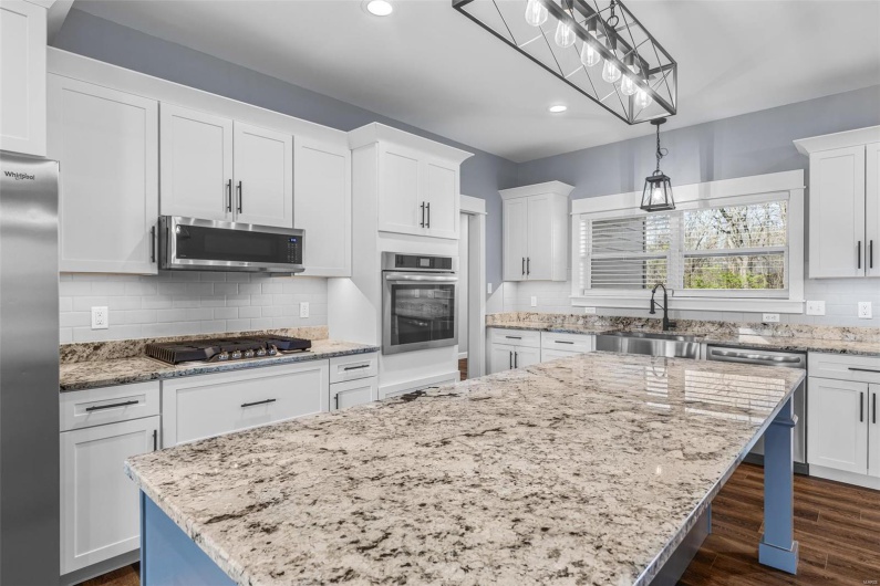 Kitchen with stainless steel appliances, dark wood-type flooring, a kitchen island, a sink, and white cabinets