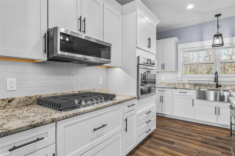 Kitchen with light stone counters, a sink, white cabinetry, appliances with stainless steel finishes, and dark wood-style flooring