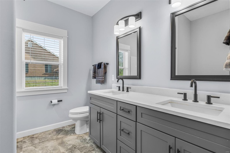 Full bathroom featuring toilet, a sink, double vanity, and baseboards