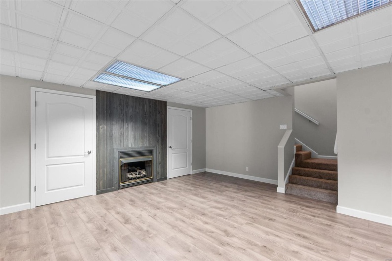 Unfurnished living room featuring a fireplace, wood walls, light hardwood / wood-style floors, and a paneled ceiling