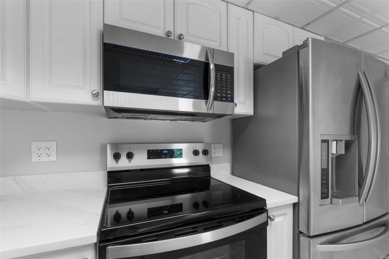 Kitchen with stainless steel appliances, white cabinets, and light stone counters