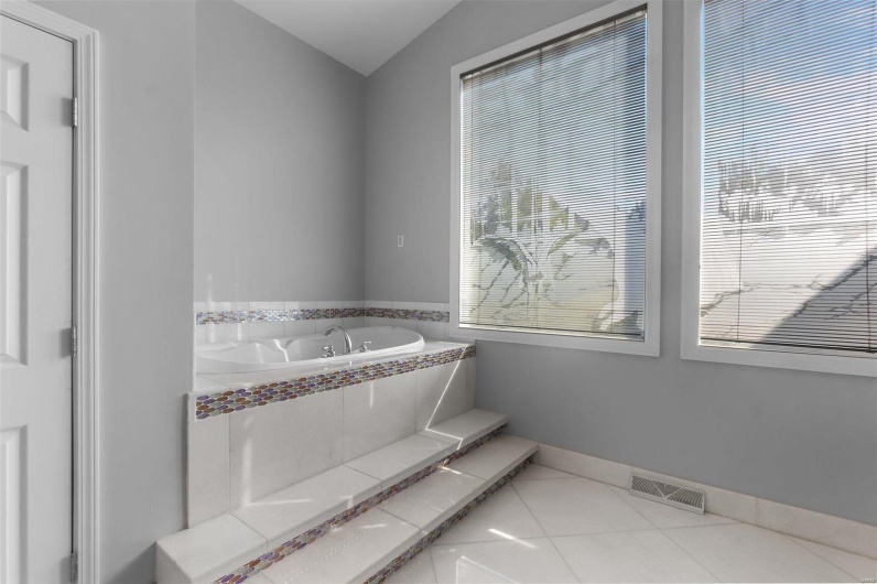 Bathroom with tile patterned floors, a relaxing tiled tub, and vaulted ceiling