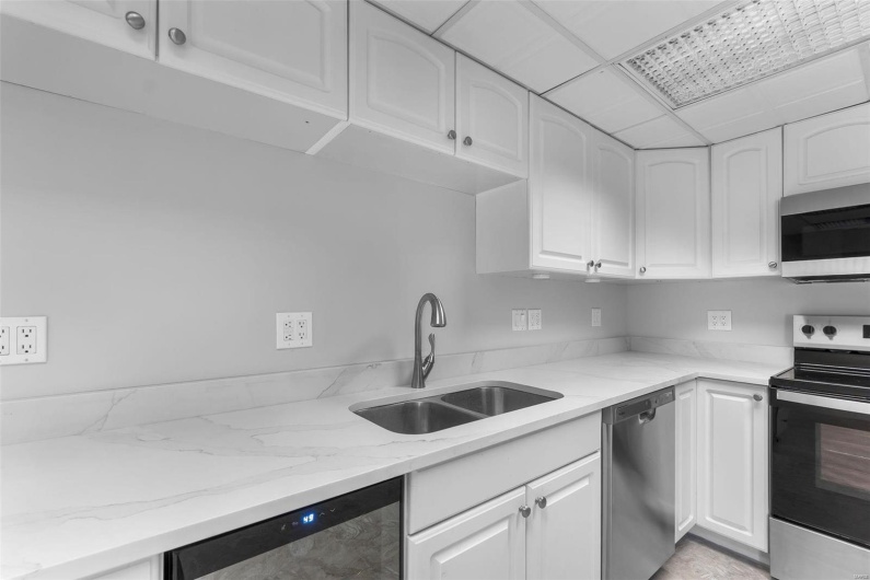 Kitchen with white cabinets, appliances with stainless steel finishes, sink, and light stone countertops