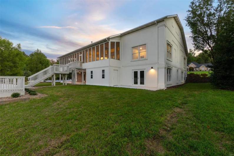 Back house at dusk with a wooden deck and a lawn