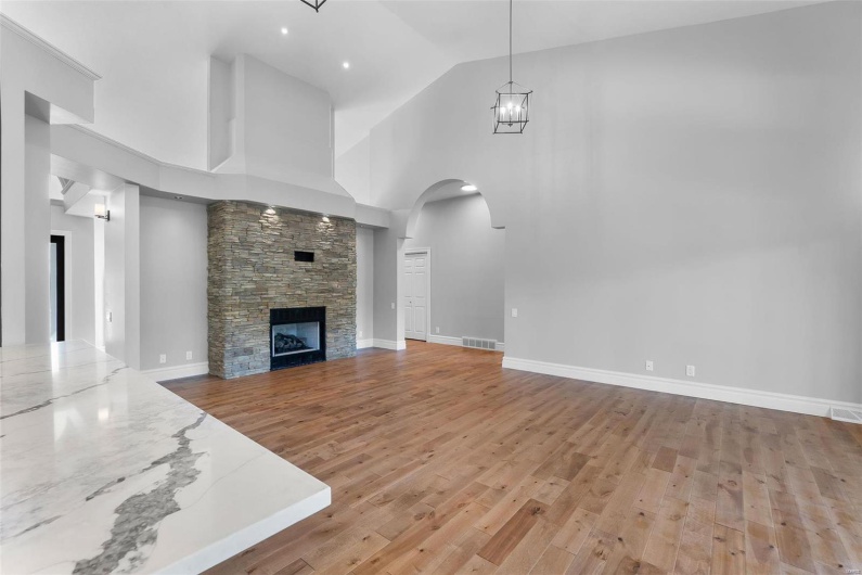 Unfurnished living room featuring a stone fireplace, an inviting chandelier, light wood-type flooring, and high vaulted ceiling