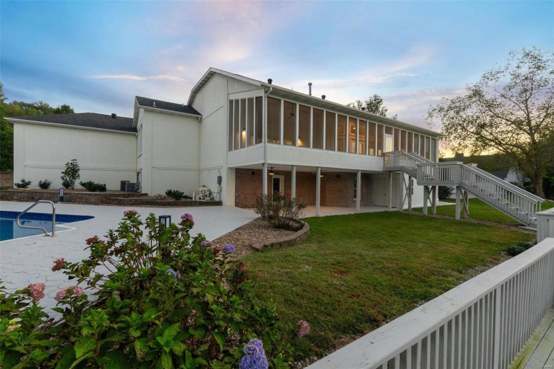 Back house at dusk featuring a patio, a sunroom, a lawn, and a swimming pool side deck