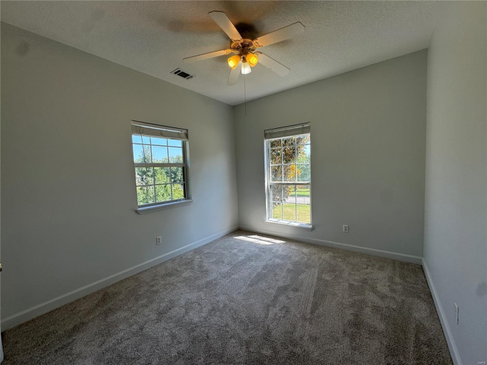 Carpeted spare room with a wealth of natural light, a textured ceiling, ceiling fan, and visible vents