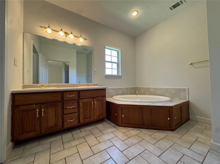 Full bath with a textured ceiling, a sink, a garden tub, visible vents, and double vanity