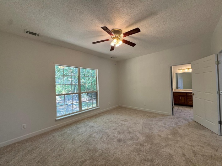 Unfurnished bedroom with baseboards, a textured ceiling, connected bathroom, visible vents, and light carpet