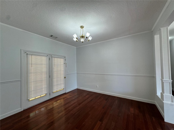Spare room featuring a chandelier, wood finished floors, a textured ceiling, visible vents, and ornamental molding