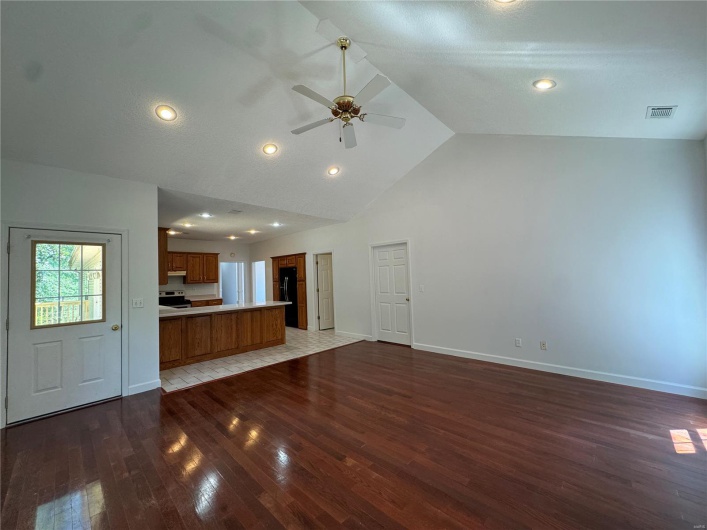 Unfurnished living room featuring high vaulted ceiling, visible vents, baseboards, wood finished floors, and a ceiling fan