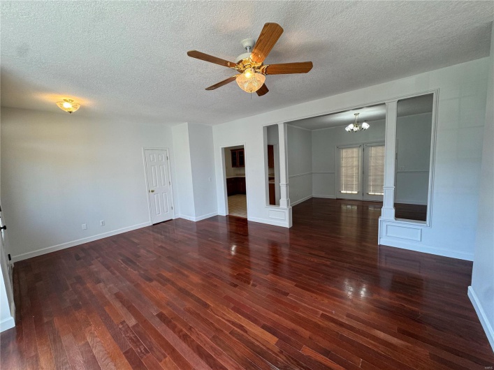 Unfurnished room with ceiling fan with notable chandelier, decorative columns, wood finished floors, and a textured ceiling