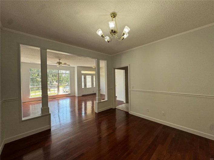 Unfurnished dining area featuring dark wood-type flooring, a textured ceiling, baseboards, and ornamental molding