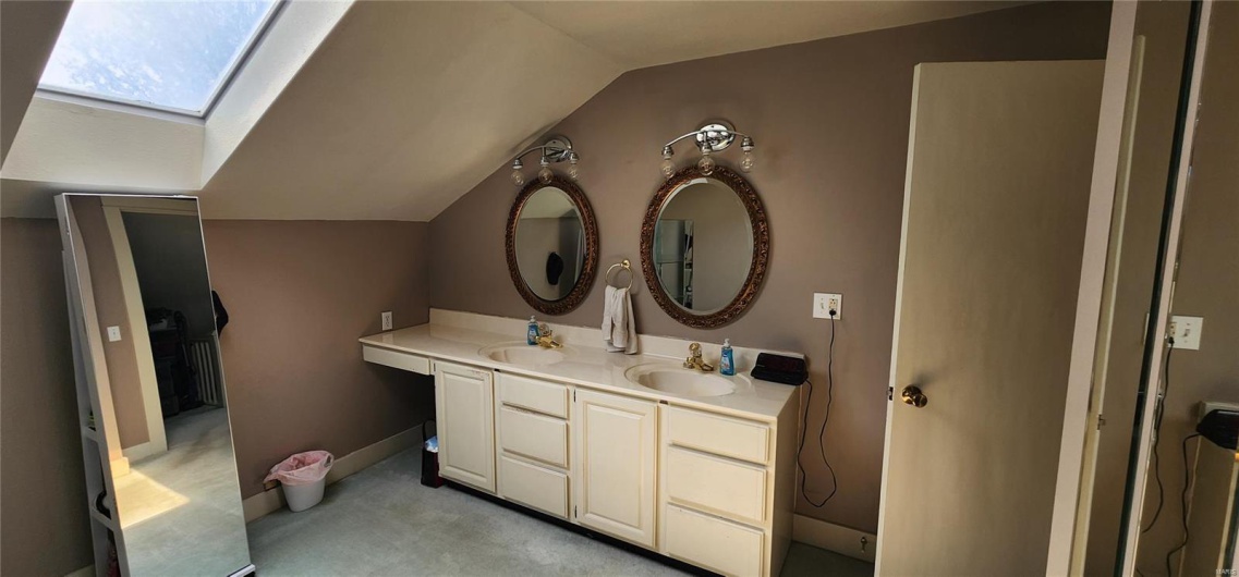 Bathroom with baseboards, double vanity, a sink, and vaulted ceiling with skylight