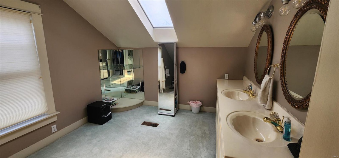 Full bath with baseboards, double vanity, lofted ceiling with skylight, and a sink