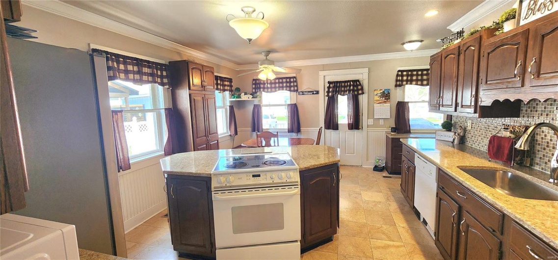 Kitchen with crown molding, a sink, a ceiling fan, and wainscoting