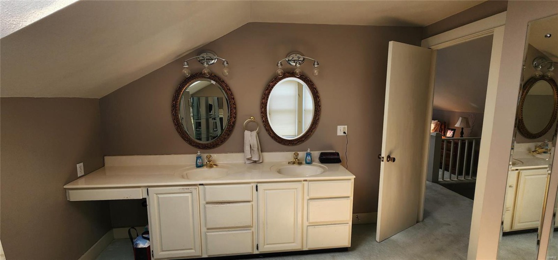 Full bathroom featuring double vanity, vaulted ceiling, and a sink