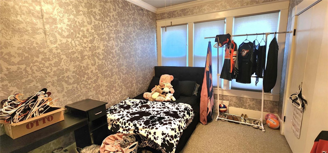 Bedroom featuring wallpapered walls, crown molding, and carpet floors