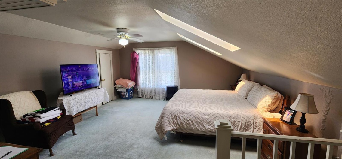 Carpeted bedroom featuring a ceiling fan, lofted ceiling with skylight, and a textured ceiling