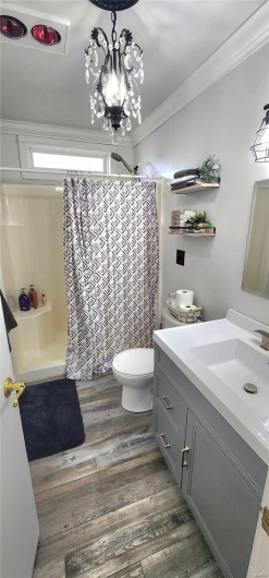 Bathroom featuring toilet, curtained shower, vanity, wood finished floors, and ornamental molding