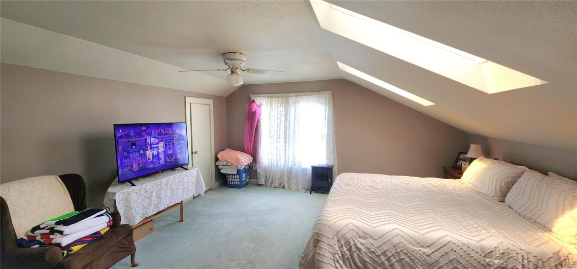 Carpeted bedroom with a textured ceiling, ceiling fan, and lofted ceiling with skylight