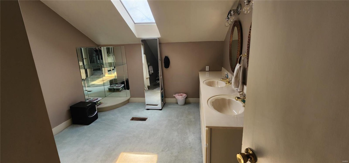 Bathroom with lofted ceiling with skylight, a sink, double vanity, and baseboards