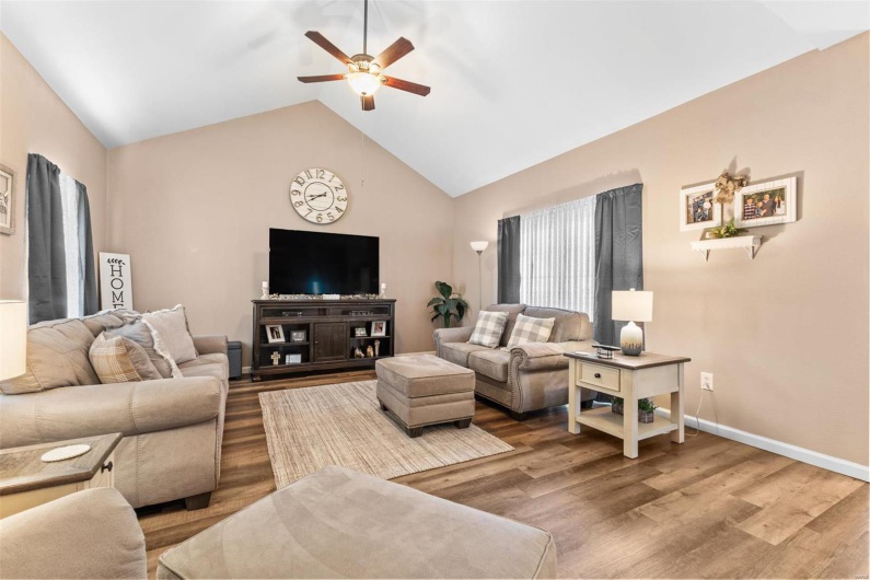Living room with ceiling fan, wood finished floors, baseboards, and vaulted ceiling