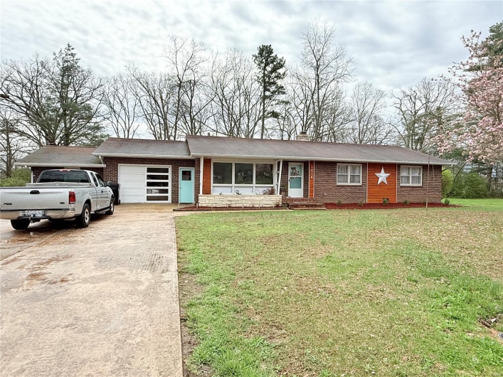 View of front facade with concrete driveway, a front yard, brick siding, a garage, and a chimney