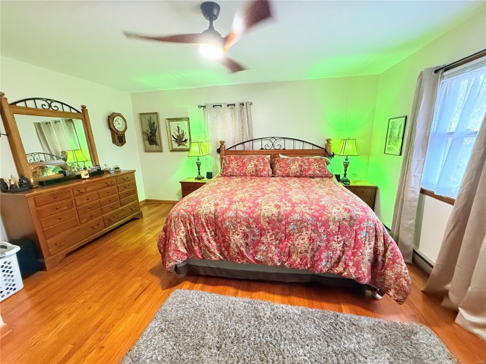 Bedroom featuring wood finished floors, ceiling fan, and a baseboard heating unit