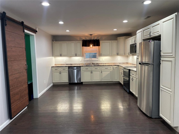 Kitchen with stainless steel appliances, a barn door, sink, dark hardwood / wood-style floors, and pendant lighting