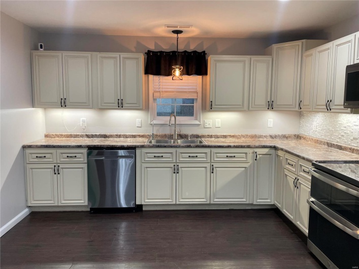 Kitchen with white cabinetry, stainless steel appliances, hanging light fixtures, dark hardwood / wood-style flooring, and sink