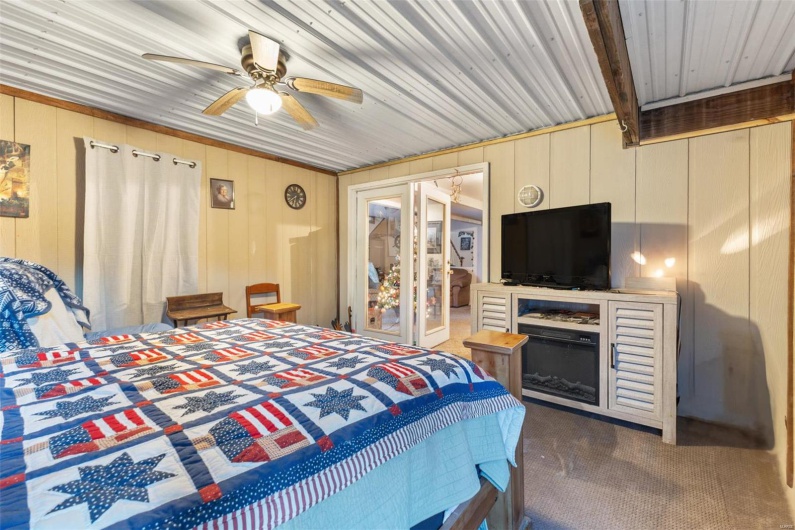 Carpeted bedroom with beam ceiling, ceiling fan, and wood walls