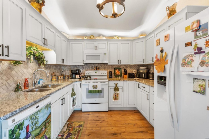 Kitchen with light wood-type flooring, light stone counters, white appliances, sink, and white cabinets