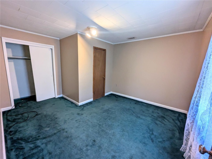 Unfurnished bedroom featuring crown molding, a closet, baseboards, dark colored carpet, and visible vents